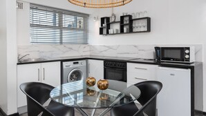Una cucina moderna con tavolo da pranzo in vetro, sedie nere, forno a incasso, microonde e lavatrice.