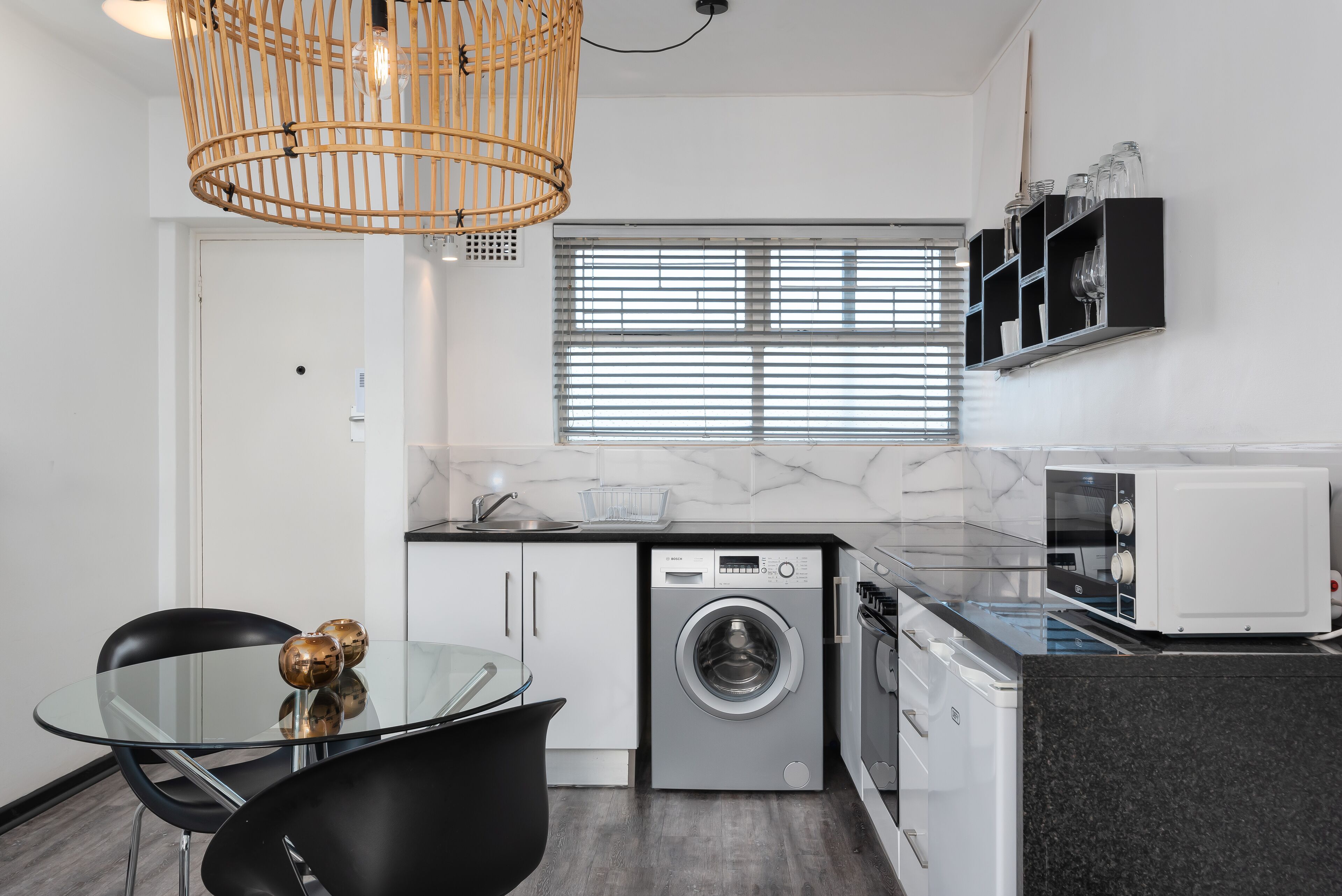 A modern kitchen with a washing machine, microwave, and a glass dining table with chairs.