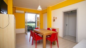 Zona pranzo con tavolo di legno e sedie rosse, lampada a soffitto bianca e porta che dà su un balcone.