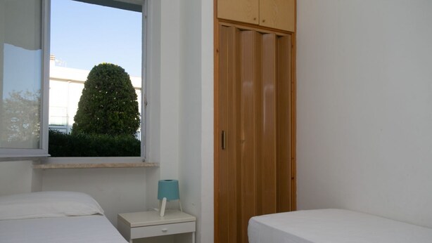 Una camera da letto con due letti, una finestra, un armadio in legno e un comodino con una lampada.