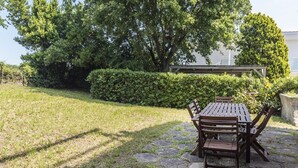 Patio esterno con tavolo e sedie in legno, immerso nel verde, tra prato e alberi.