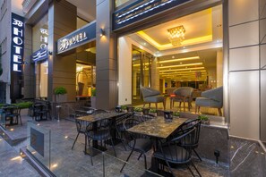 An outdoor seating area with tables and chairs, a glass partition, and a sign for a hotel.
