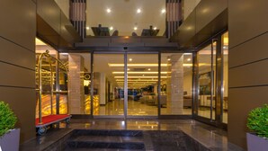Une entrée d’hôtel moderne avec une porte en verre, un tapis rouge et un chariot.