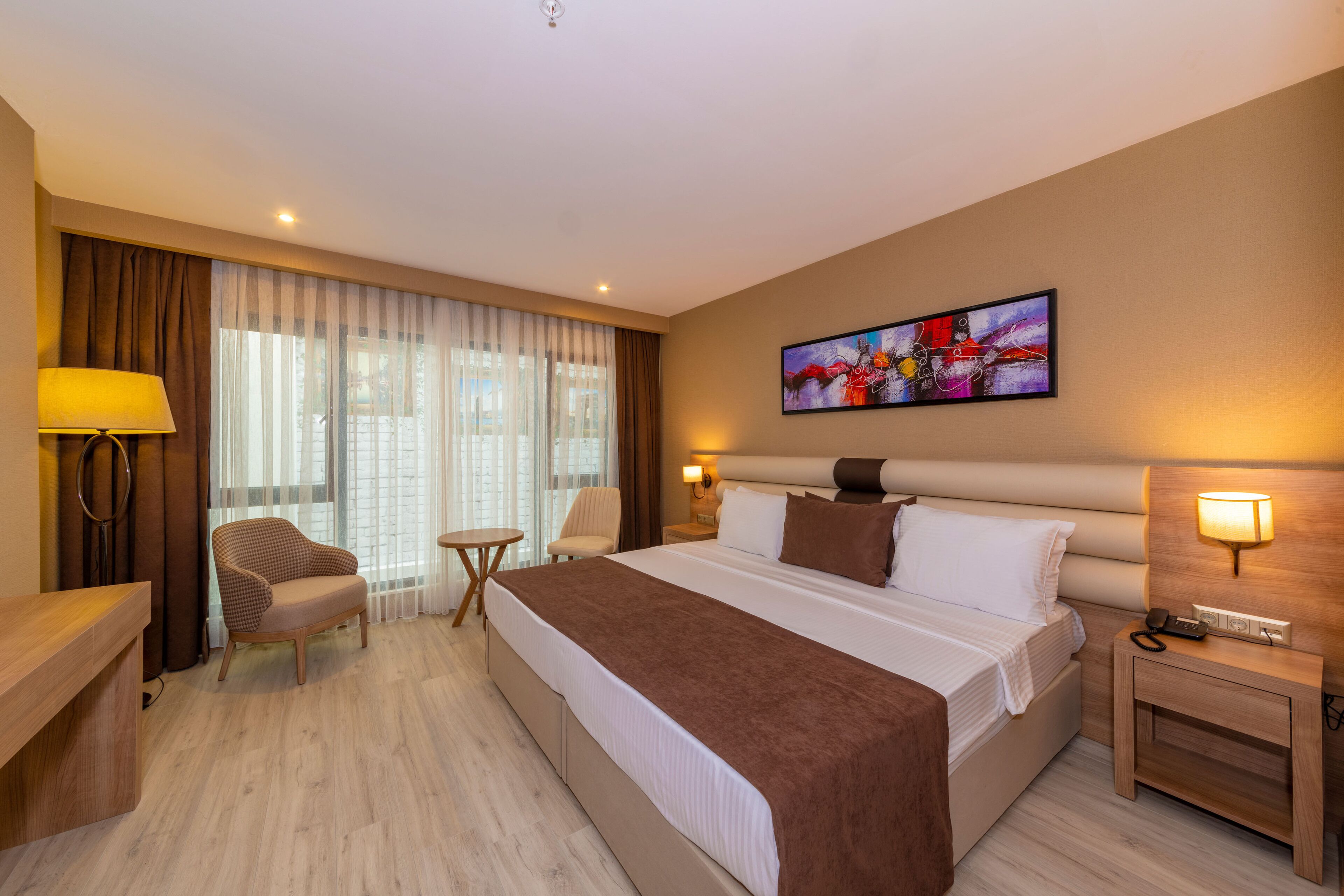 A hotel room with a large bed, a desk, a chair, a small table, and a painting on the wall.