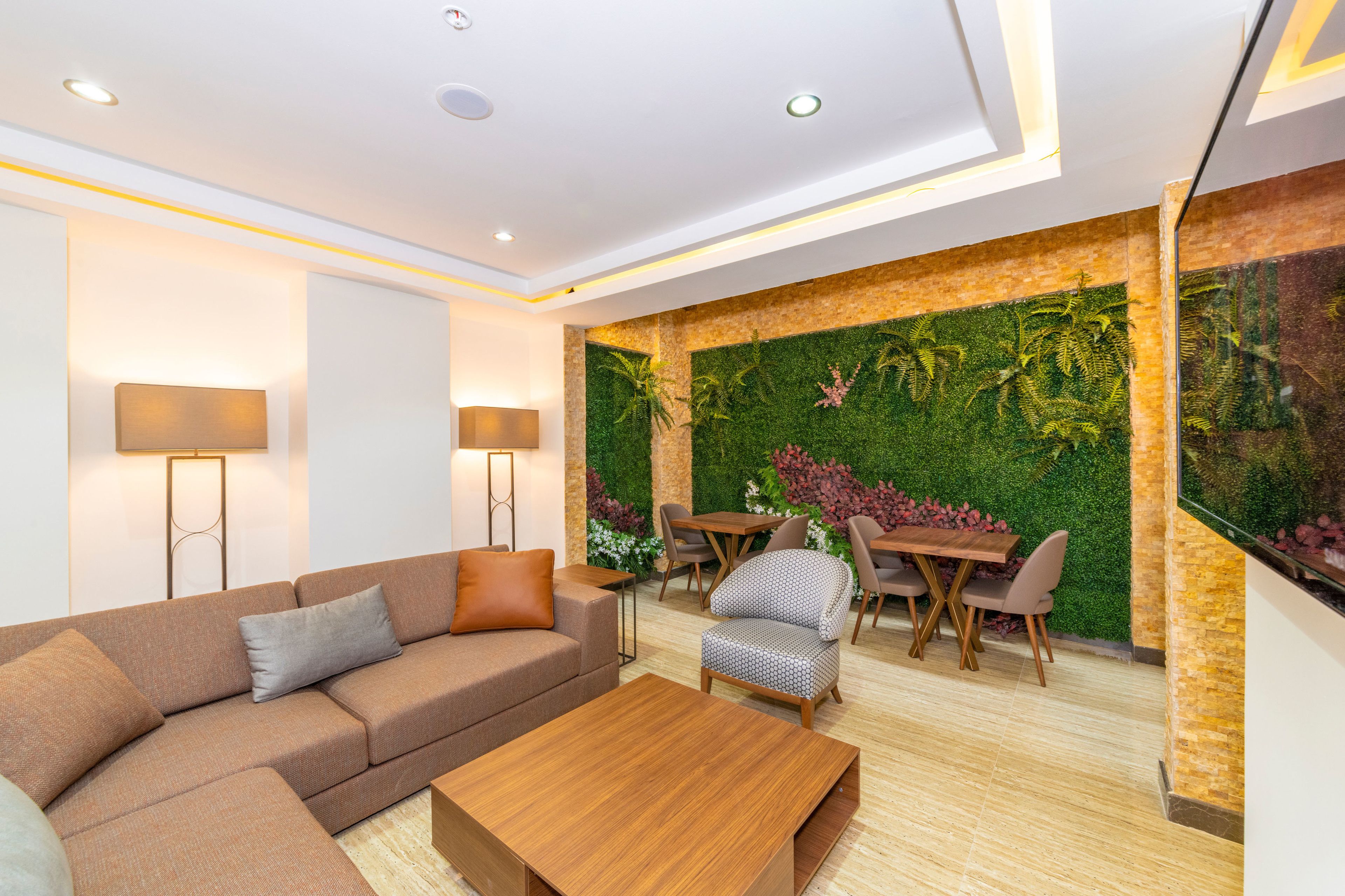 Una sala moderna con un sofá modular, una mesa de centro de madera, un comedor con mesa y sillas, y una pared verde con jardín vertical.