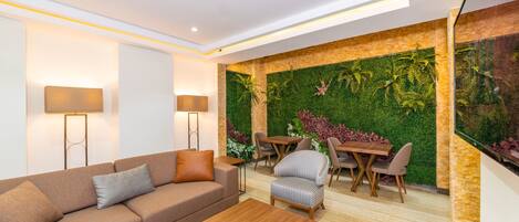 Una sala moderna con un sofá modular, una mesa de centro de madera, un comedor con mesa y sillas, y una pared verde con jardín vertical.