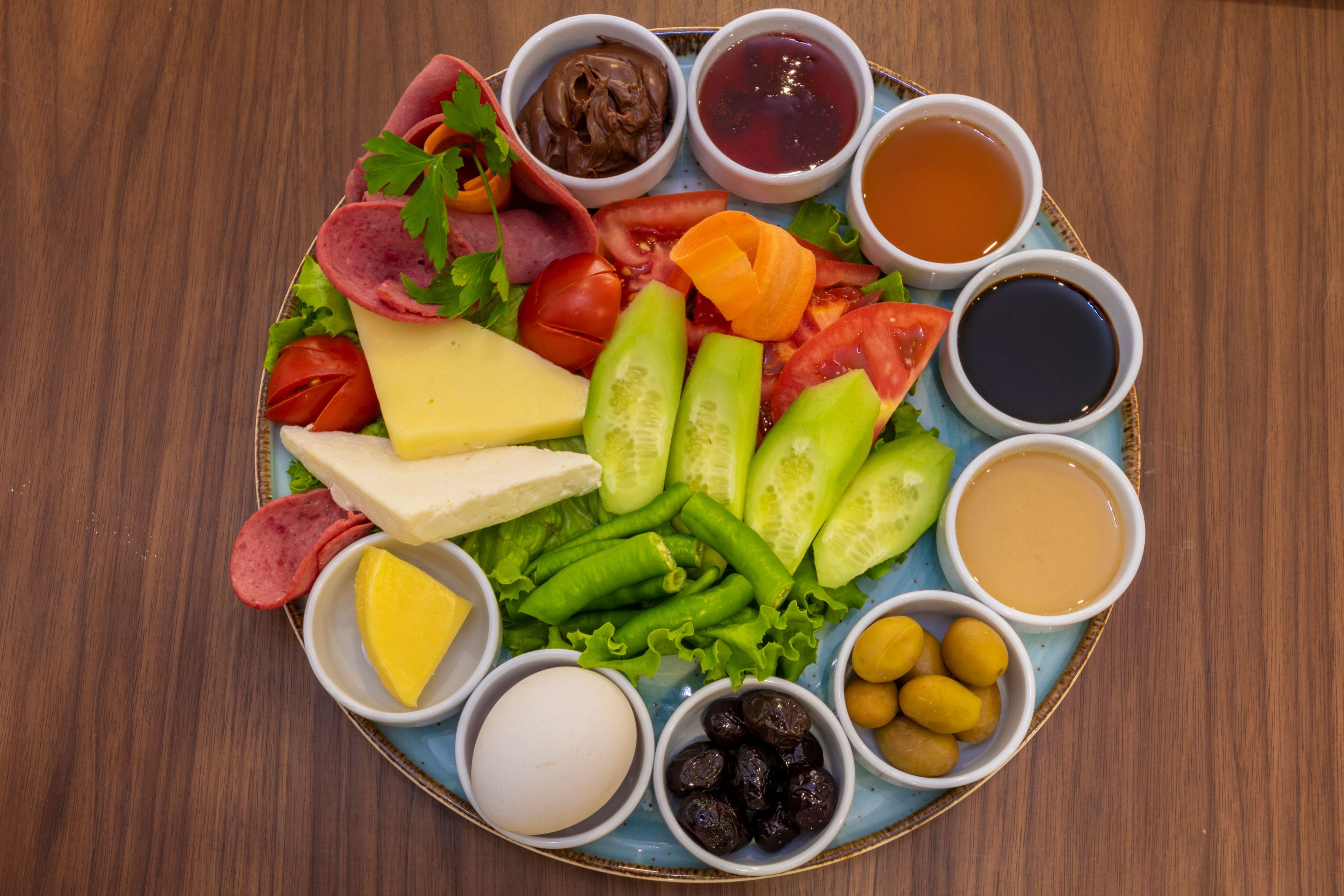 Una bandeja con quesos, embutidos, verduras y salsas.