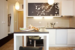 A modern kitchen with a dining area, featuring a wooden table, a black chair, a white cabinet, and a black and white wall art piece.