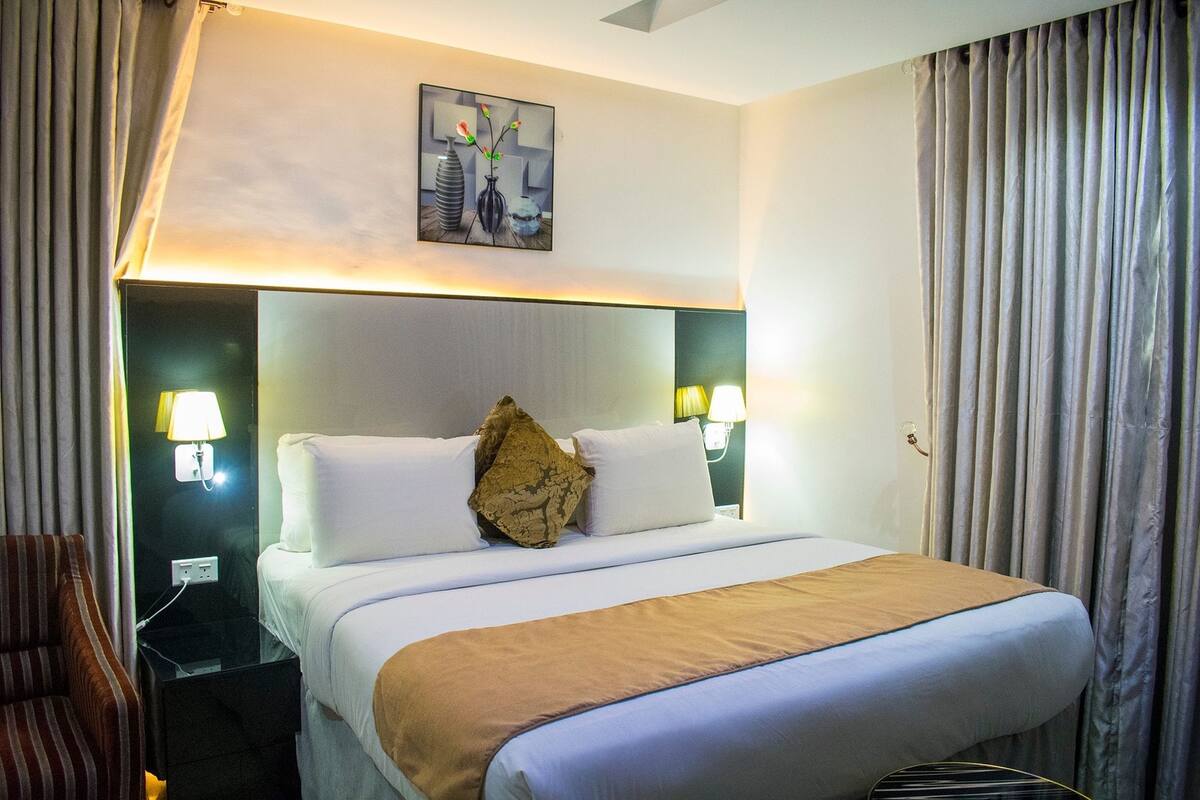 A hotel room with a large bed, two bedside lamps, a nightstand, a chair, and a painting on the wall.