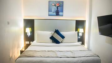 A hotel room with a large bed, two bedside lamps, a flat-screen TV, and a painting above the bed.