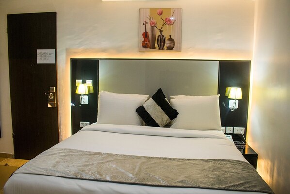 Quarto de hotel com uma cama grande, duas luminárias de cabeceira, uma mesa de apoio e um quadro pendurado na parede.