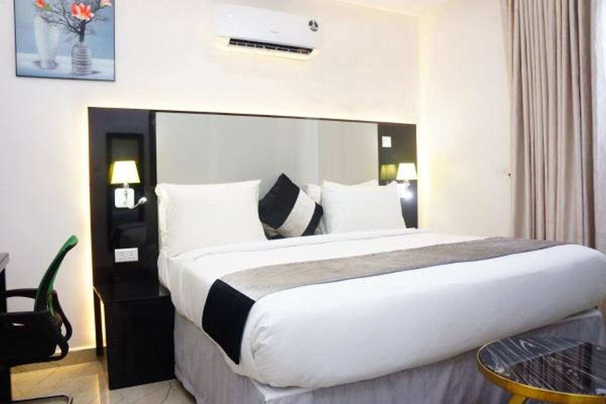 A hotel room with a large bed, bedside tables with lamps, a small round table, and a painting on the wall.