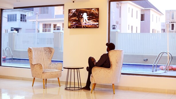 A modern hotel room with a large window, a television, two armchairs, and a small round table. - Ziroc Residence (Lekki)