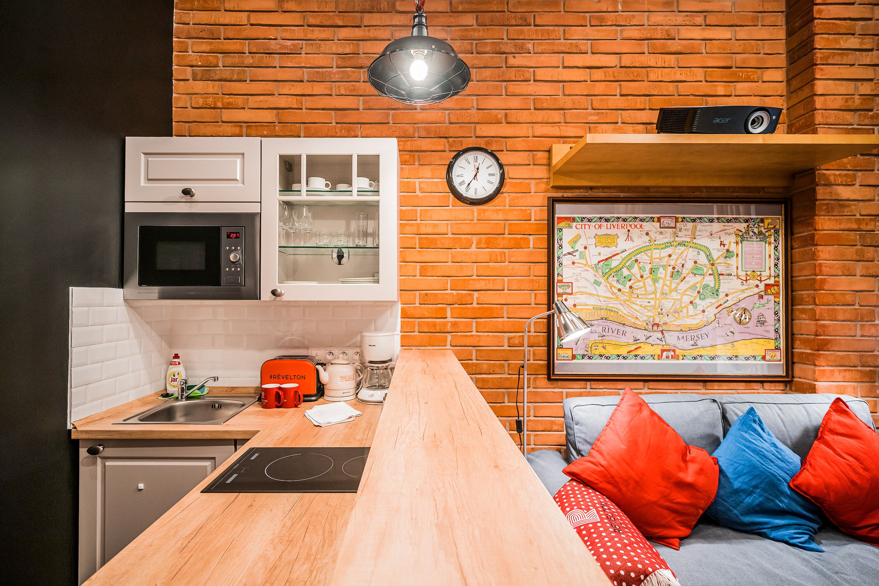 A kitchen with a microwave, oven, and coffee maker, a wooden countertop, and a brick wall.