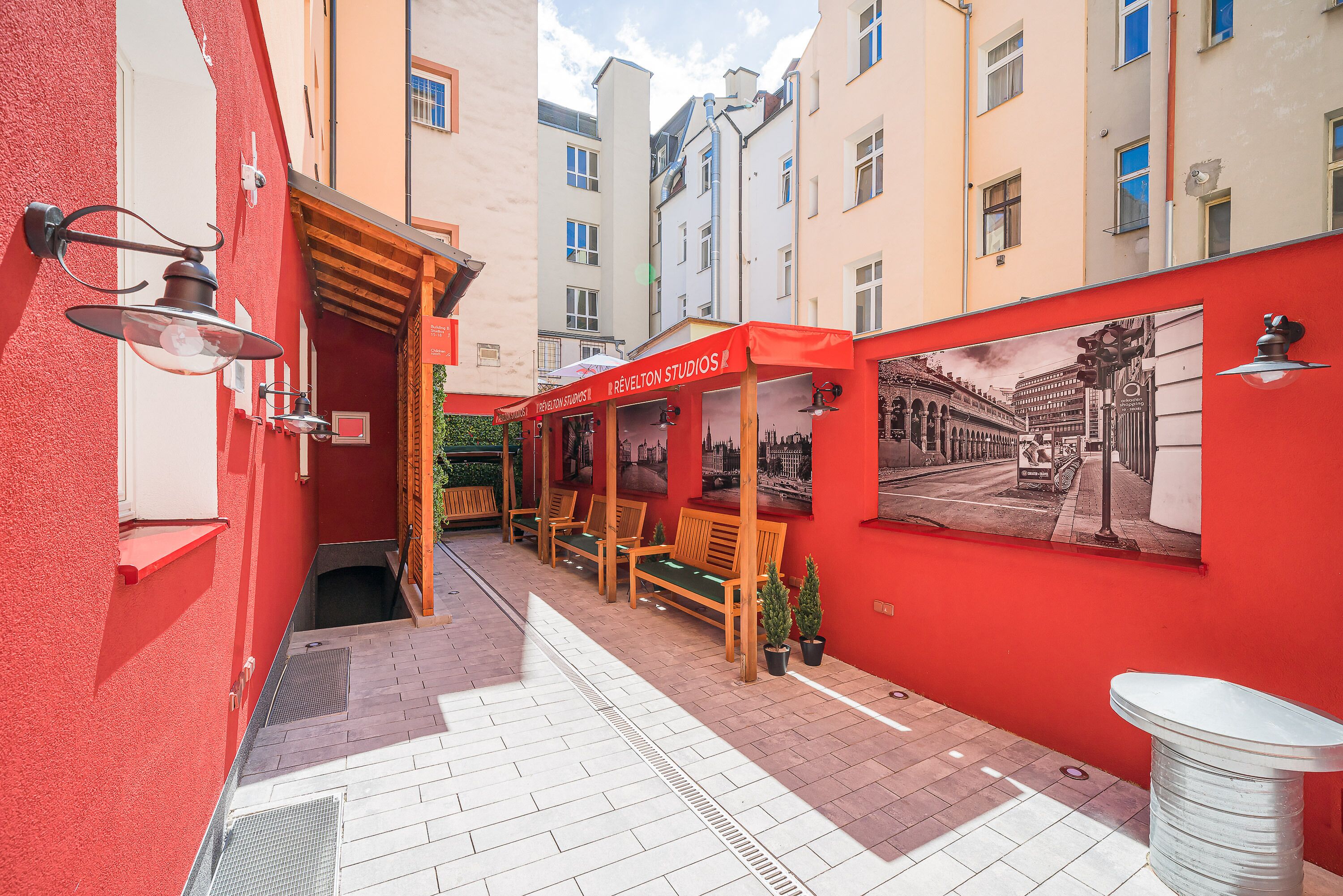 A narrow alleyway with a red building on the left, a wooden bench area with a sign for 'Revelton Studios', and a mural on the right wall.