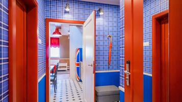 Un couloir étroit aux murs à carreaux bleus et blancs, avec des portes rouges et un banc.