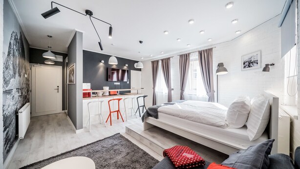 A modern bedroom with a bed, a desk, and a kitchenette.