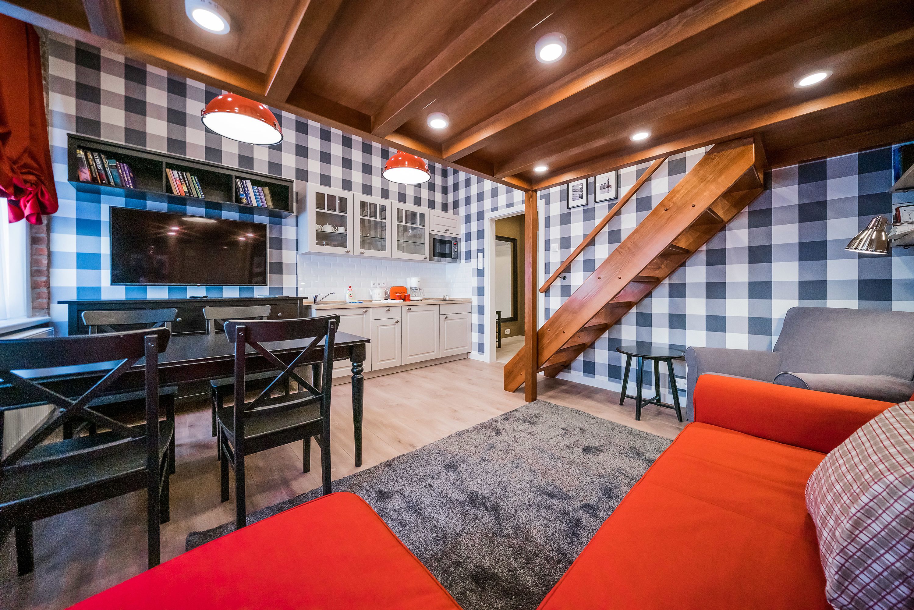 Una cocina moderna con salpicadero de cuadros, vigas de techo de madera y un comedor con televisor y estanterías.