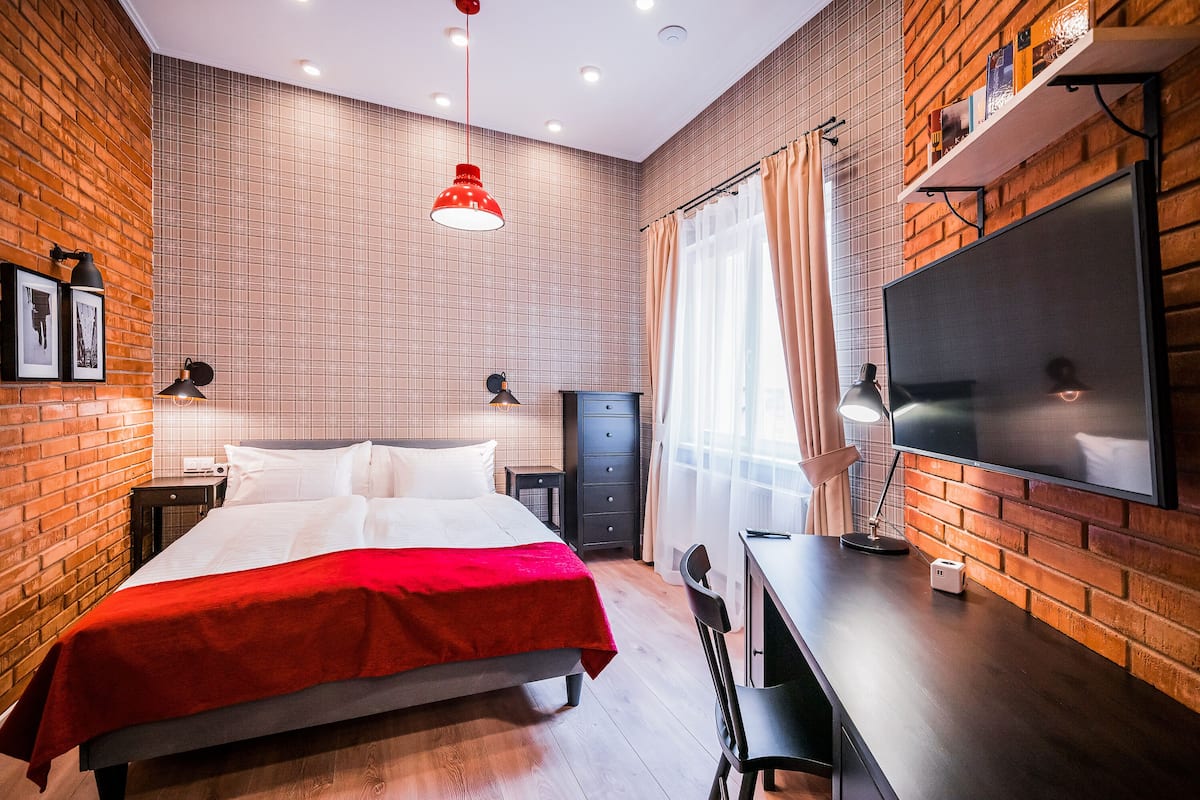 Une chambre d’hôtel avec un lit, un bureau, une télévision et des murs en briques.