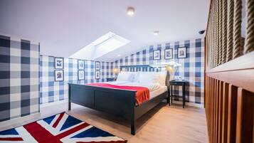 A bedroom with a bed, a desk, a chair, a lamp, and a skylight.