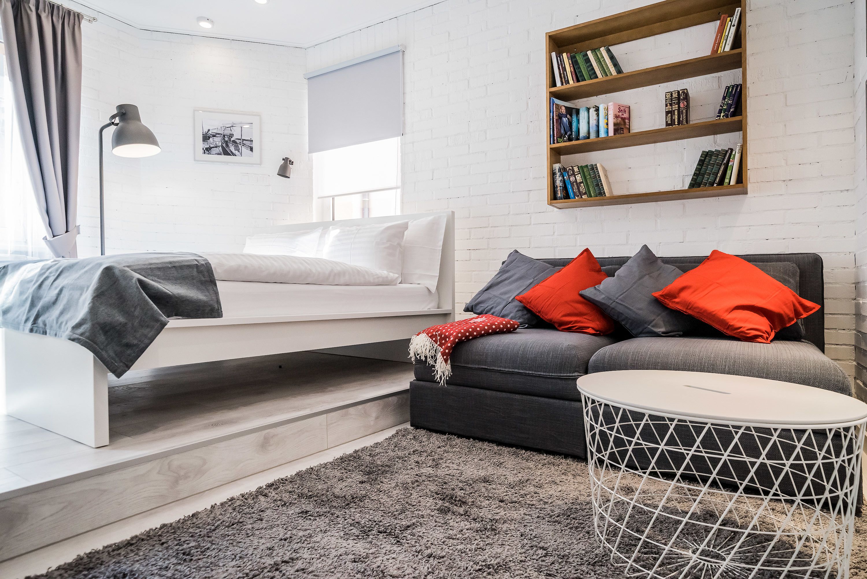 A modern living room with a sofa, a small round table, a bookshelf, and a bed.
