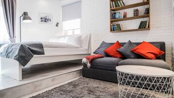 A modern living room with a sofa, a small round table, a bookshelf, and a bed.