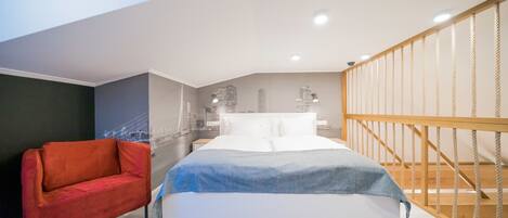 A modern bedroom with a bed, a red chair, a wooden staircase, and a cityscape mural on the wall.