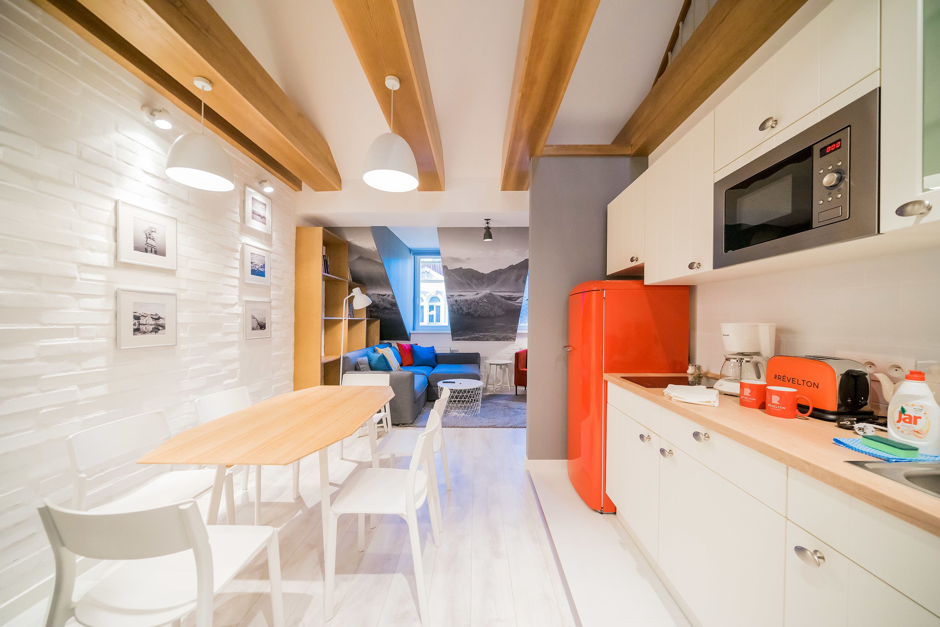 A modern kitchen with a microwave, coffee maker, and orange refrigerator.