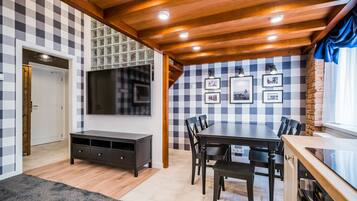 Een eetruimte met een houten plafond, een geruit wandpaneel en een grote flatscreen televisie bevestigd boven een donker houten tafel en stoelen.