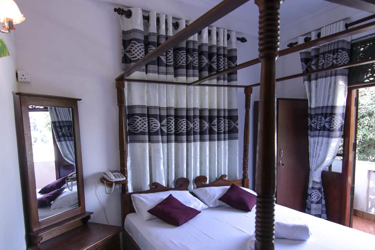 A four-poster bed with a wooden frame, a ceiling fan, patterned curtains, and a bedside telephone.