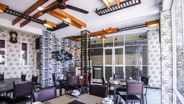 Un restaurante con una decoración moderna, que presenta vigas de madera a la vista, papel tapiz estampado y una variedad de opciones de asientos.