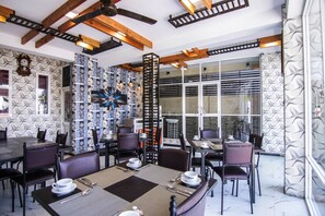 A restaurant with a modern interior, featuring exposed wooden beams, patterned wallpaper, and a mix of seating arrangements.