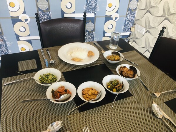 A dining table set with various dishes, including rice, vegetables, and meat, in a room with patterned wallpaper and a black leather chair.