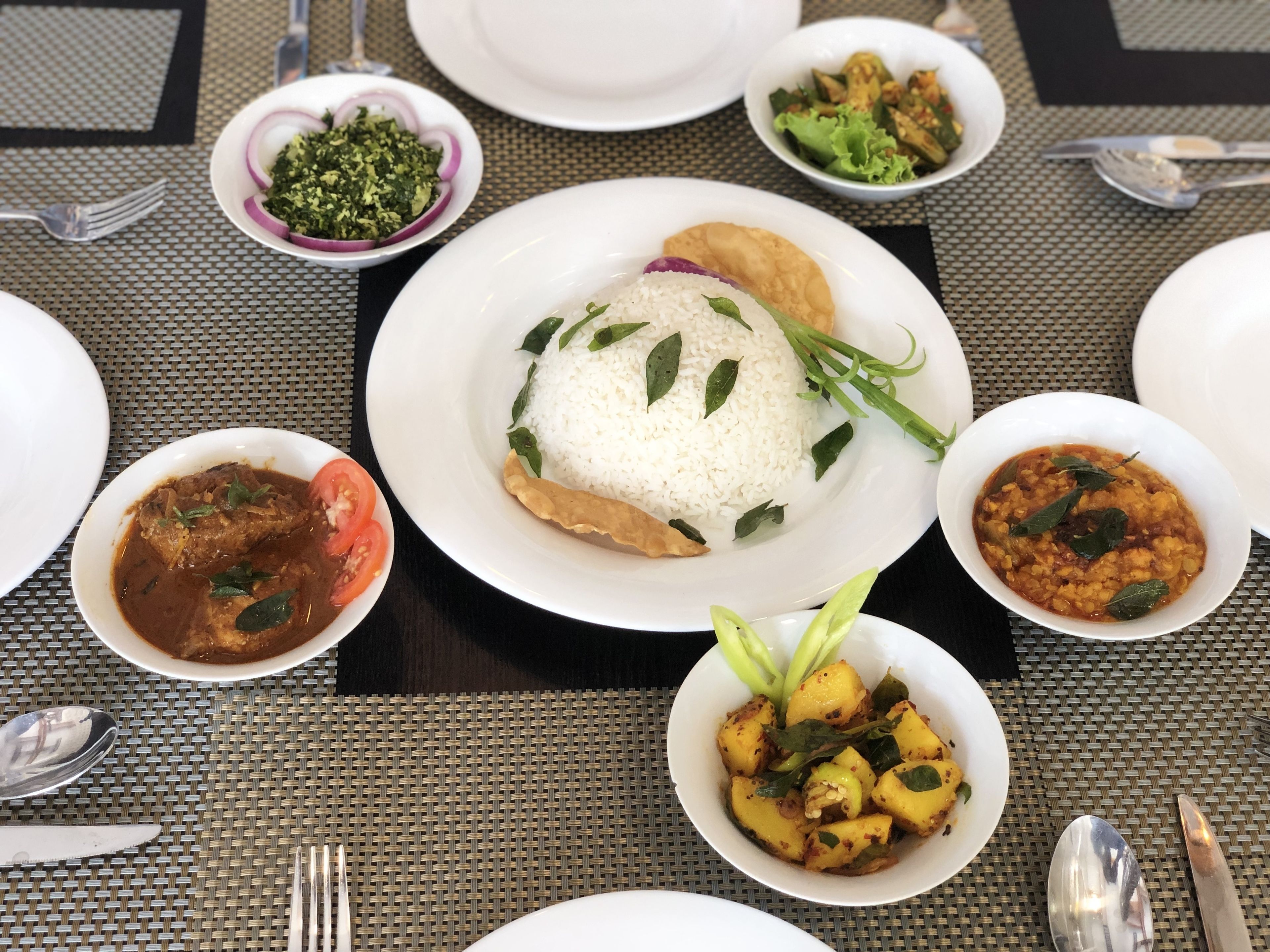 Ein Tisch ist reichhaltig mit verschiedenen Speisen gedeckt, darunter Reis, Curry und Gemüse.