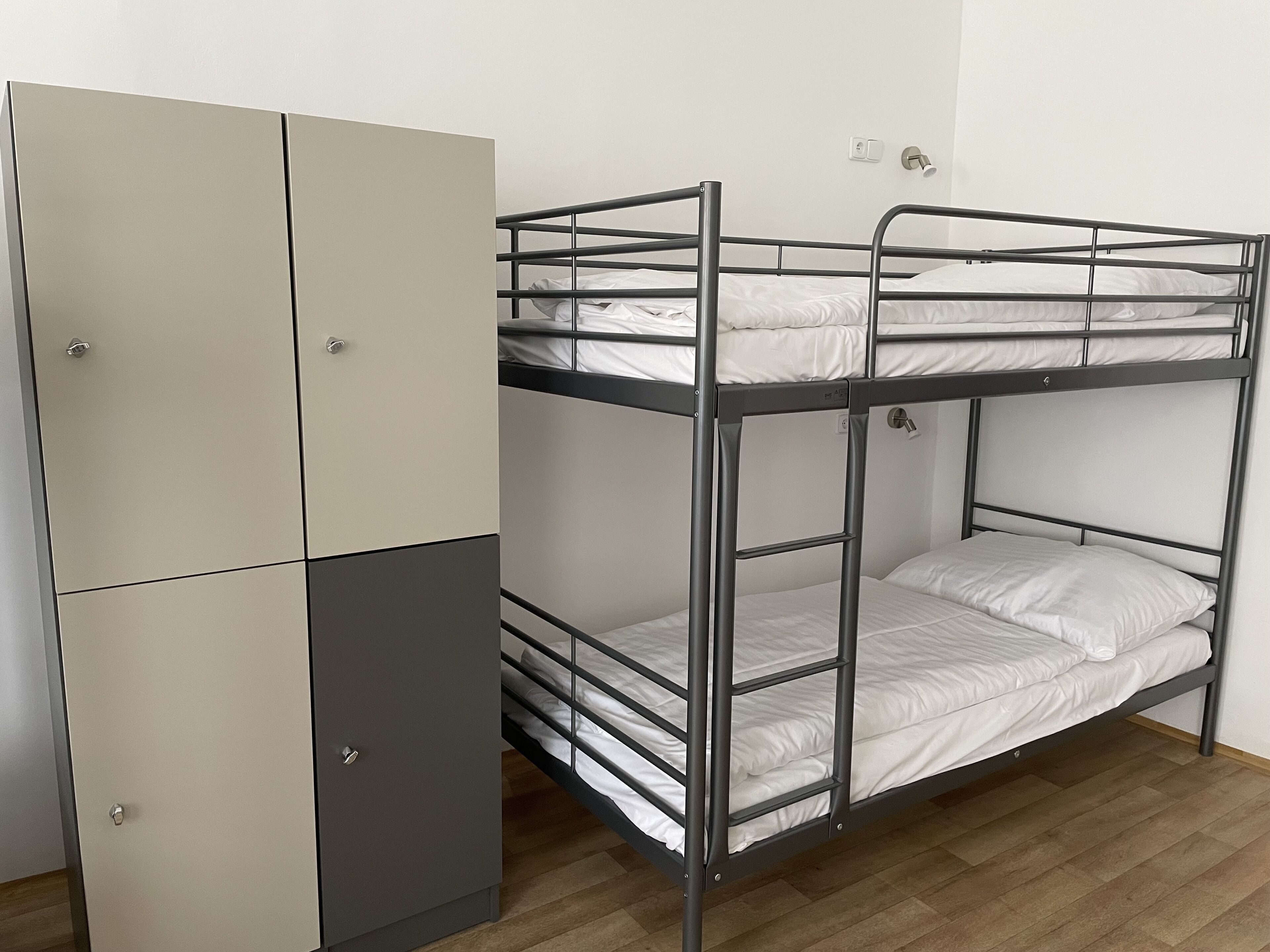 Una cama litera con un armario, suelo de madera y un interruptor de luz en la pared.