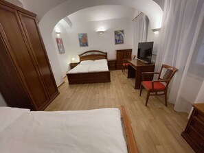 A hotel room with a bed, a desk, a chair, a TV, and a wardrobe.