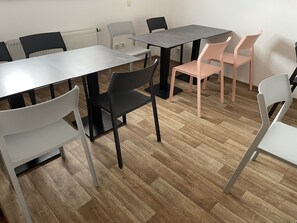 A room with a wooden floor, white and black chairs, and a grey table.