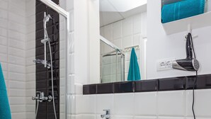 Ein Badezimmer mit Dusche, Waschbecken und Toilette. Handtücher befinden sich an einem Haken, ein Fön ist an der Wand befestigt.
