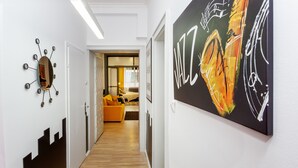 Ein Flur mit modernem Design, der ein Spiegel mit einem besonderen Muster, ein großes abstraktes Gemälde und einen Holzboden zeigt, der zu einem Wohnbereich mit einer Couch und einem Couchtisch führt.