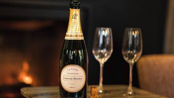 A bottle of champagne, a cork, and two glasses on a wooden table.