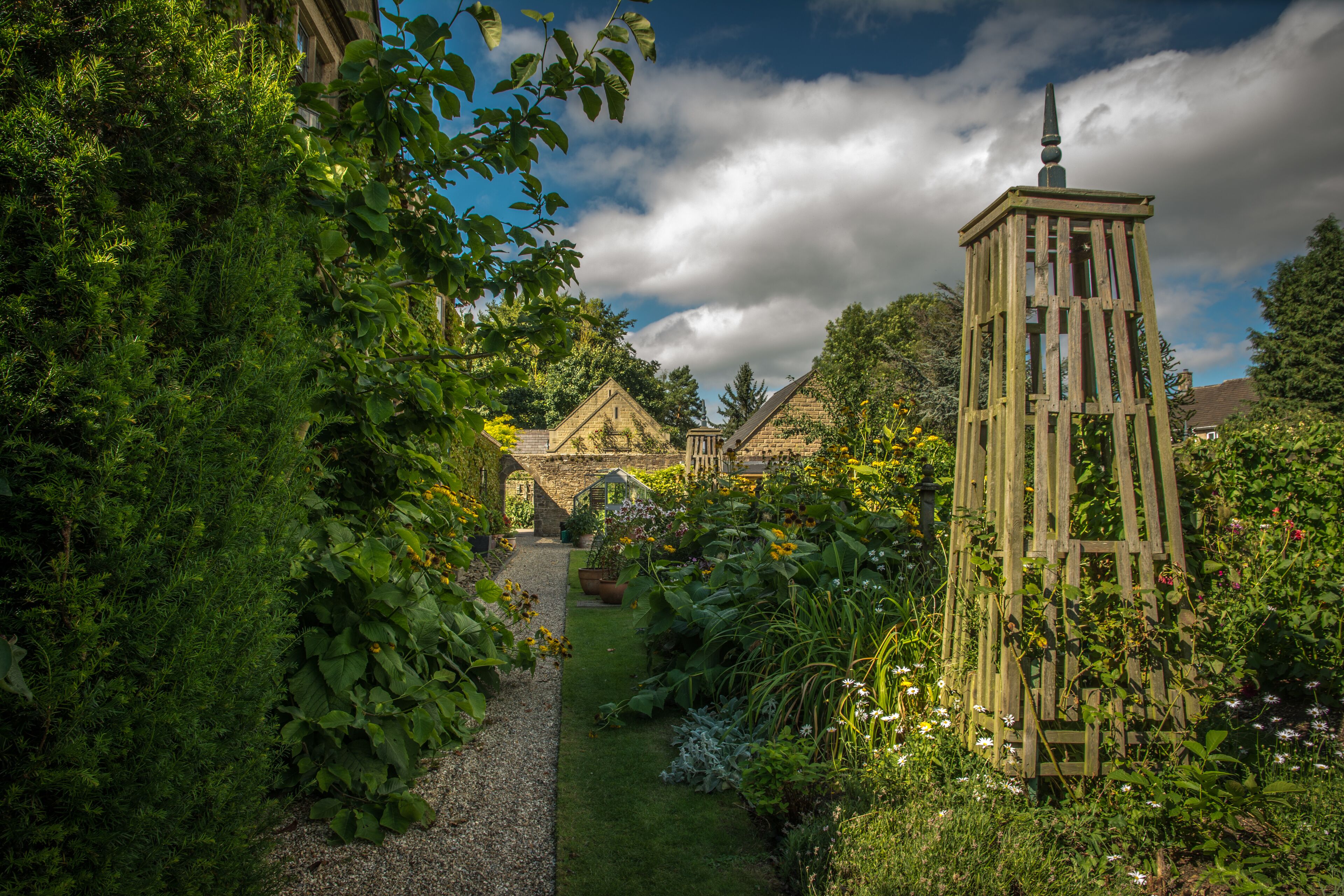 Un jardin agrémenté d’une tour en bois, d’un bâtiment en pierre et d’une végétation luxuriante.