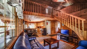 A spacious living area with a large leather sofa, a wooden coffee table, and a television. A wooden staircase leads to an upper level.