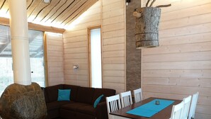 A cozy room with a wooden floor, a brown sofa with blue cushions, a dining table with white chairs, and a stone fireplace.