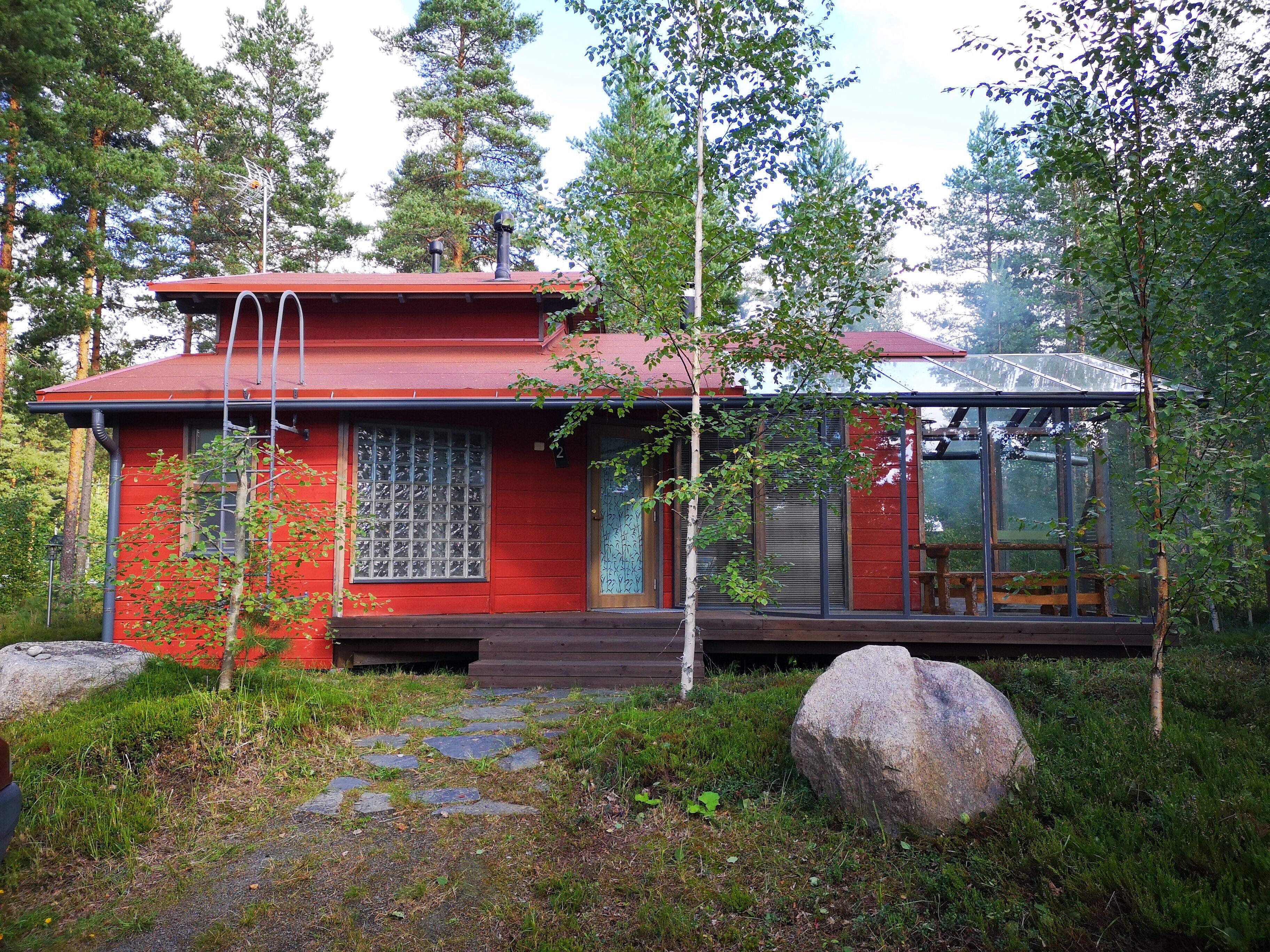 A red cabin with a glass extension, surrounded by trees and rocks.