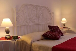 A neatly made bed with a decorative headboard, two bedside tables with lamps, and a red patterned pillow. - Vesta Domus (Rome)