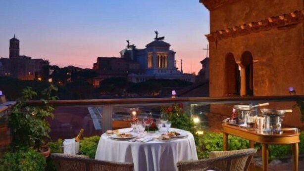 An outdoor dining area with a table set for two, overlooking a cityscape at dusk. - Vesta Domus (Rome)