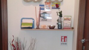 A hallway with a 'Coffee' sign, a Wi-Fi zone sign, a clock, and a fire safety sign. There are potted plants and a small shelf with various items. - Vesta Domus (Rome)