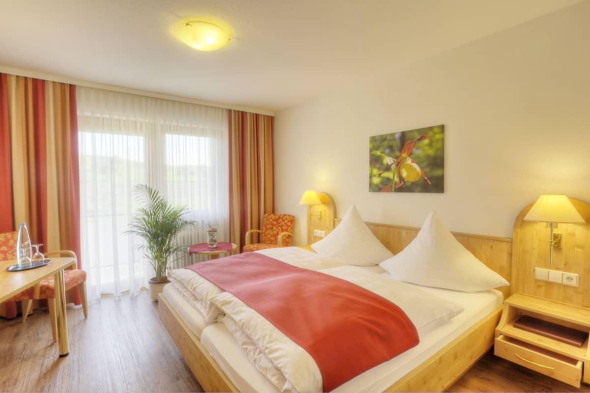 A hotel room with a bed, a desk, a chair, a lamp, and a plant.