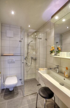 A modern bathroom with a glass-enclosed shower, a toilet, a sink with a mirror, and a stool. - Pension Fohrenberg (Wutach)