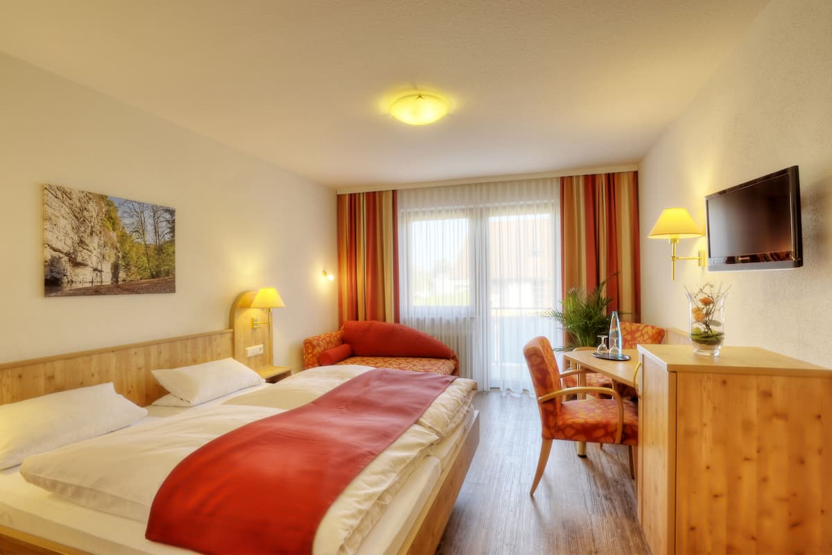 A hotel room with a bed, a desk, a chair, a TV, and a window with curtains.